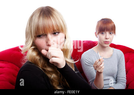 Jeune et belle blonde aux cheveux rouge filles sur canapé rouge fumeurs in front of white background Banque D'Images