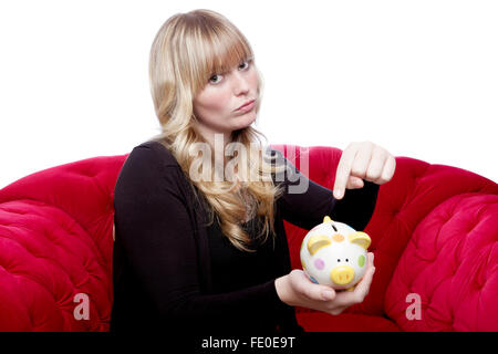 Jeune fille aux cheveux blonds veulent de l'argent dans sa tirelire sur canapé rouge in front of white background Banque D'Images