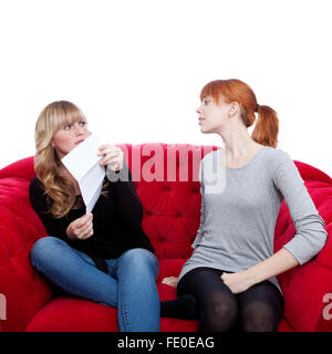 Jeune et belle blonde aux cheveux rouges pour cacher lettre sur canapé rouge in front of white background Banque D'Images