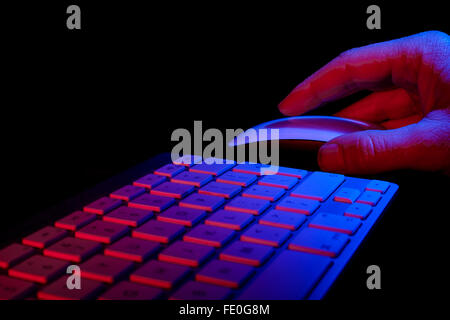 Clavier et souris Apple avec la main de l'homme sur la souris. Éclairé par la lumière bleue et rouge. Banque D'Images