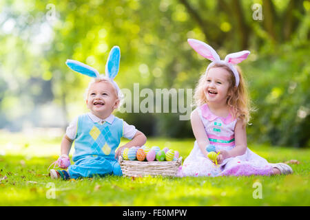 Petit garçon et fille s'amusant sur chasse aux œufs de Pâques. Kids in Bunny Ears et costume de lapin. Les enfants avec des oeufs colorés Banque D'Images