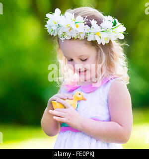 Petite fille s'amusant sur chasse aux œufs de Pâques. Kid en jouant avec la couronne de fleurs canard ou poulet. Les enfants à la recherche d'oeufs Banque D'Images