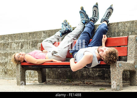 Les jeunes gens fatigués en fonction de la formation d'amis avec des patins à roulettes. La femme et l'homme couché sur banc de la piscine de détente. Banque D'Images