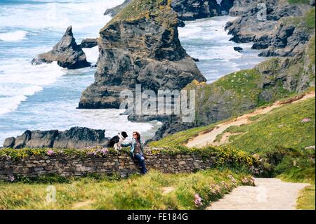 Les piles de la mer falaises au Bedruthan Steps sur le South West Coast Path près de Newquay, Cornwall, Angleterre. Femme et chien border collie Banque D'Images