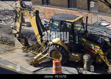 Travailleur de la construction l'exploitation d'une pelleteuse jaune faites par la société Caterpillar c'est creuser dans une rue de la ville Banque D'Images