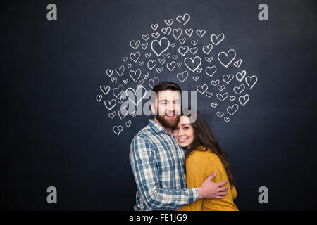Happy young couple hugging and debout sur tableau noir derrière eux Banque D'Images