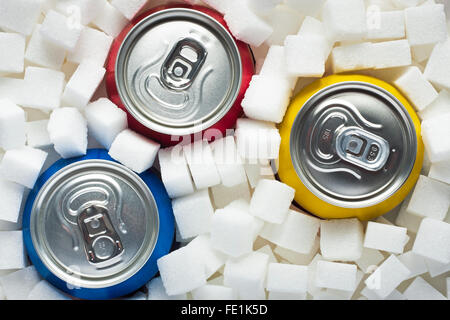 Concept d'aliments malsains - le sucre dans les boissons gazeuses. Le sucre en cubes comme arrière-plan et des boissons en conserve Banque D'Images