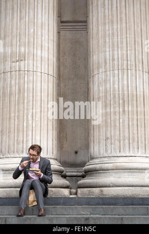 Un homme assis en train de manger son déjeuner sur les marches de la cathédrale St Paul à Londres Banque D'Images