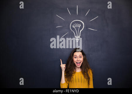 Cheerful young woman with a ouvert la bouche dirigée vers le haut et avoir une idée sur l'arrière-plan tableau noir Banque D'Images