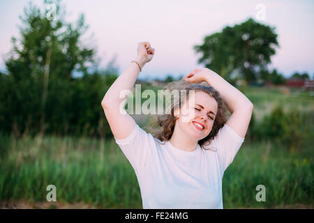 Pretty Caucasian Grande Taille jeune femme en chemise blanche dansant sur fond vert prairie d'été sur le terrain. L'été, piscine Portrait Banque D'Images