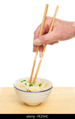Main tenant les baguettes dans un bol de riz frit à l'oeuf sur une table contre un fond blanc Banque D'Images