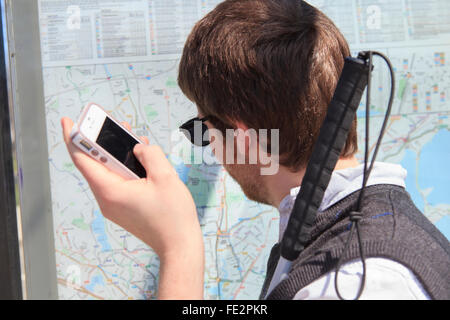 Jeune homme aveugle à un arrêt d'autobus à l'aide de technologies d'aide à la carte Banque D'Images