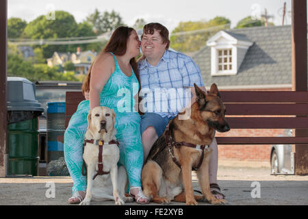 Jeune couple ayant une déficience visuelle et les chiens assis sur un banc et de dire un secret Banque D'Images