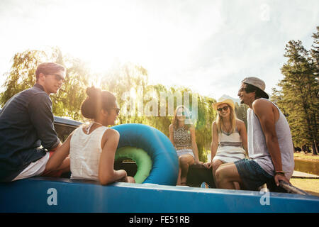 Groupe de jeunes amis assis à l'arrière d'une camionnette avec des tubes gonflables passe un été de congé sur une journée ensoleillée. Banque D'Images