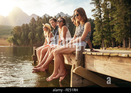 Portrait de groupe de jeunes gens assis sur le bord d'une jetée, à l'extérieur dans la nature. Les amis passer une journée au bord du lac. Banque D'Images