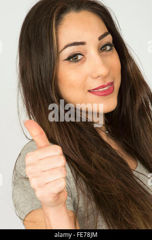 Young dark haired woman smiling giving Thumbs up hand gesture Banque D'Images