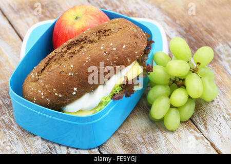 Boîte à lunch saine contenant brown rouleau avec fromage et œuf dur et laitue, pomme rouge et raisins sur rustique en surfa Banque D'Images