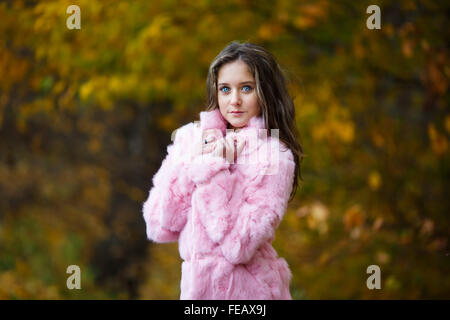 Portrait de belle fille dans un manteau de fourrure rose sur un fond de feuilles jaunes Banque D'Images