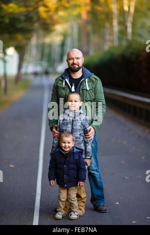 Père avec deux fils debout sur la route dans un parc, au temps d'automne Banque D'Images
