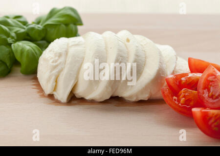 Tranches de mozzarella fraîche avec des feuilles de basilic et les tomates sur planche de bois Banque D'Images