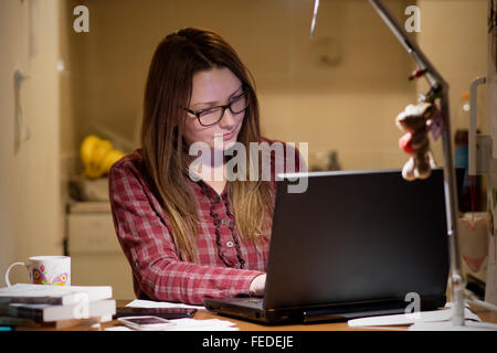 Jeune femme de payer les factures en ligne tard dans la soirée après avoir terminé tous les travaux de sa maison, assis au bureau avec ordinateur, b Banque D'Images