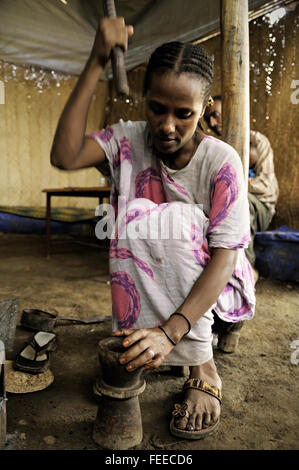Les grains de café de meulage femme à l'intérieur d'un mortier avec un pilon en bois dans Berhale, région Afar, Ethiopie Banque D'Images
