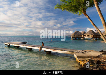 Woman sitting on jetty avec bungalows sur pilotis de l'hôtel, Le Maitai Bora Bora, îles de la société, Polynésie Française Banque D'Images