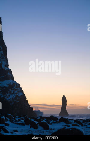 Vagues éclaboussant contre les rochers de roches basaltes Reynisdrangar à la plage de sable noir Reynisfjara au lever du soleil, en Islande du Sud en janvier Banque D'Images