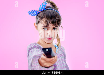 Little girl holding télécommande isolé sur fond rose Banque D'Images