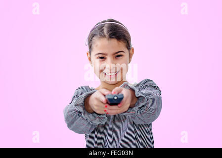 Little girl holding télécommande isolé sur fond rose Banque D'Images