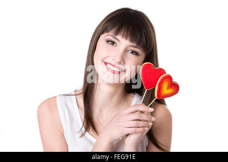 Portrait Portrait de jeune belle cheerful woman holding deux rouge en forme de coeur les cookies, studio, fond blanc, isolé Banque D'Images