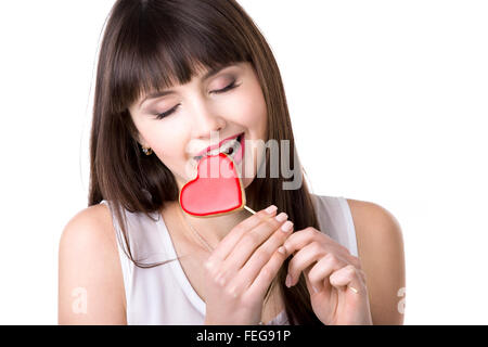 Portrait Portrait of young woman holding rouge en forme de coeur délicieux cookie, avoir une saine alimentation biscuit avec les yeux fermés Banque D'Images