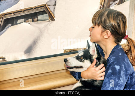 Petite fille avec le chien husky en regardant par la fenêtre Banque D'Images