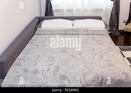 Chambre élégante avec des oreillers décoratifs blancs et les toits sur lit. Canapé dans le Salon sert de chambre à coucher Banque D'Images