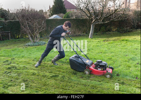 Première coupe de pelouse de l'année mal après l'hiver doux et l'herbe haute de la croissance sur une tondre le gazon avec une coupe d'essence Banque D'Images