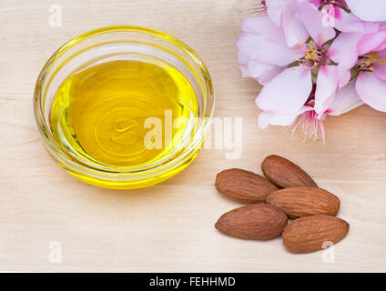 L'huile d'amandes dans un plat avec les noix et amandes jolie rose fleurs sur une surface de travail de pin Banque D'Images