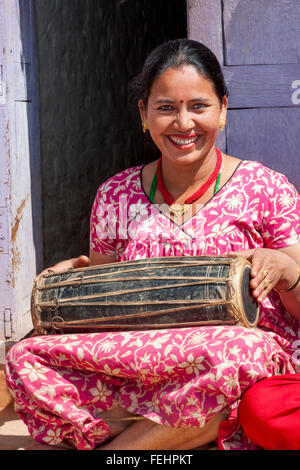 Bhaktapur, Népal. Femme jouant un tambour alors qu'il était assis avec des amis sur son porche. Banque D'Images