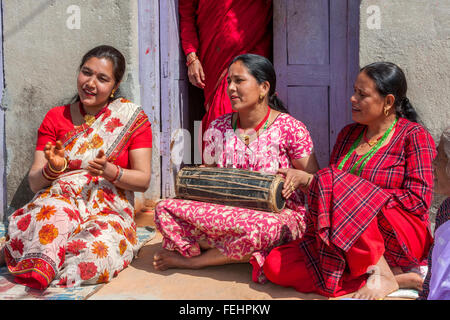 Bhaktapur, Népal. Femme jouant un tambour alors qu'il était assis avec des amis sur son porche. Banque D'Images