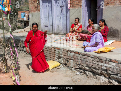 Bhaktapur, Népal. Femme d'âge moyen tandis que les amis des danses du tambour jouer et Clap, assis sur le porche avant de leur maison. Banque D'Images