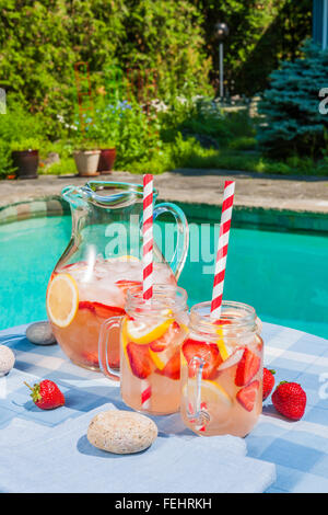 Froid de glace limonade aux fraises faites maison en pichet et verres avec paille Papier sur table côté piscine extérieure en été avec jardin à b Banque D'Images