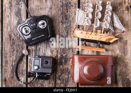 Divers jouets pour différents âges. Caméra d'action, Vieux film, commande à distance de l'appareil photo et le modèle de voilier sur fond de bois. Banque D'Images