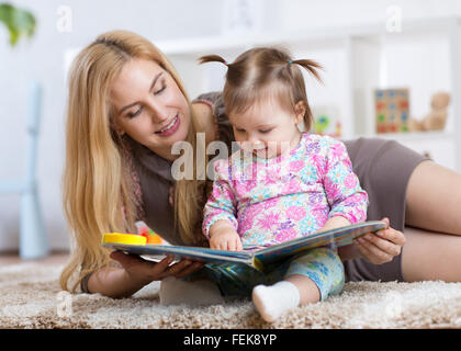 Sweet baby girl with mother reading book in nursery Banque D'Images