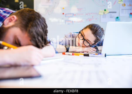 Épuisé jeune femme et l'homme dort sur la table in office Banque D'Images