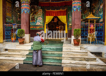 Vieille Femme portant le costume traditionnel prie en face d'un temple bouddhiste à Katmandou, Népal Banque D'Images