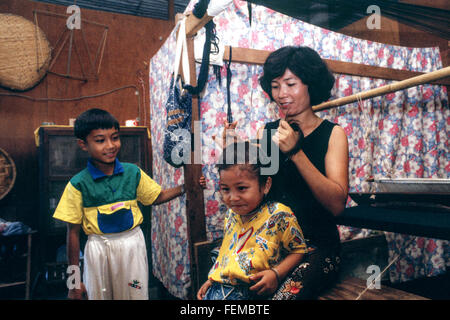 Les jeunes frère et sœur à se préparer à l'école dans leur petite maison de fortune au Laos et leur mère range la fille a les cheveux longs. Banque D'Images