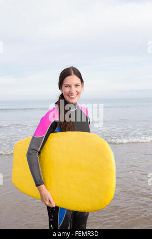 Dame posant sur la plage dans une combinaison avec un body-board. Banque D'Images