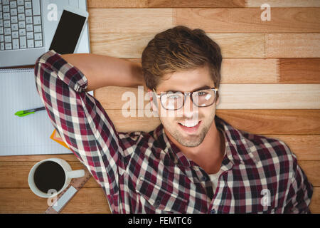 Image composite de hipster smiling while par ordinateur portable sur plancher de bois franc Banque D'Images