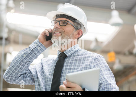 Ingénieur avec hard-hat and digital tablet talking on cell phone Banque D'Images