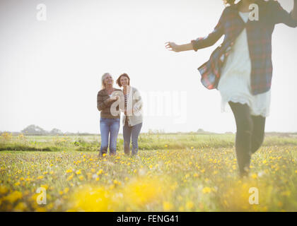 Les femmes watching girl exécuter sous le soleil de prairie avec des fleurs sauvages Banque D'Images