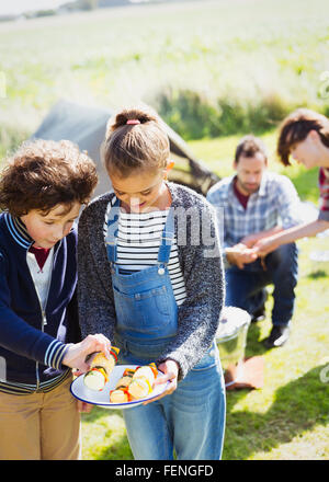 Frère et sœur à brochettes de légumes à l'ensoleillée au camping Banque D'Images